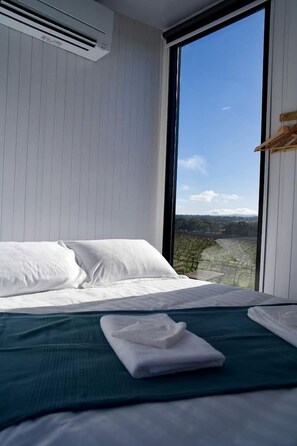 A bedroom with a large window, a bed with white bedding, and a green bedspread.