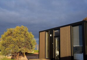 Un edificio moderno con un ingresso con porta in vetro, un letto visibile all'interno e un albero sullo sfondo.