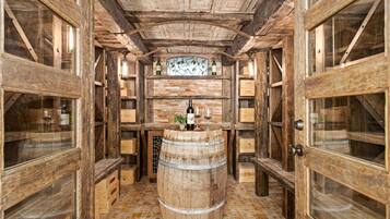 A wooden wine cellar with a barrel in the center, wooden shelves, and a wine rack above.