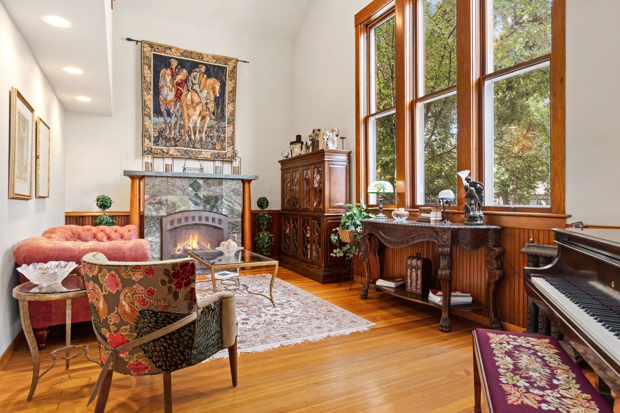 A spacious living room with a fireplace, a piano, and a large window with a view of trees.