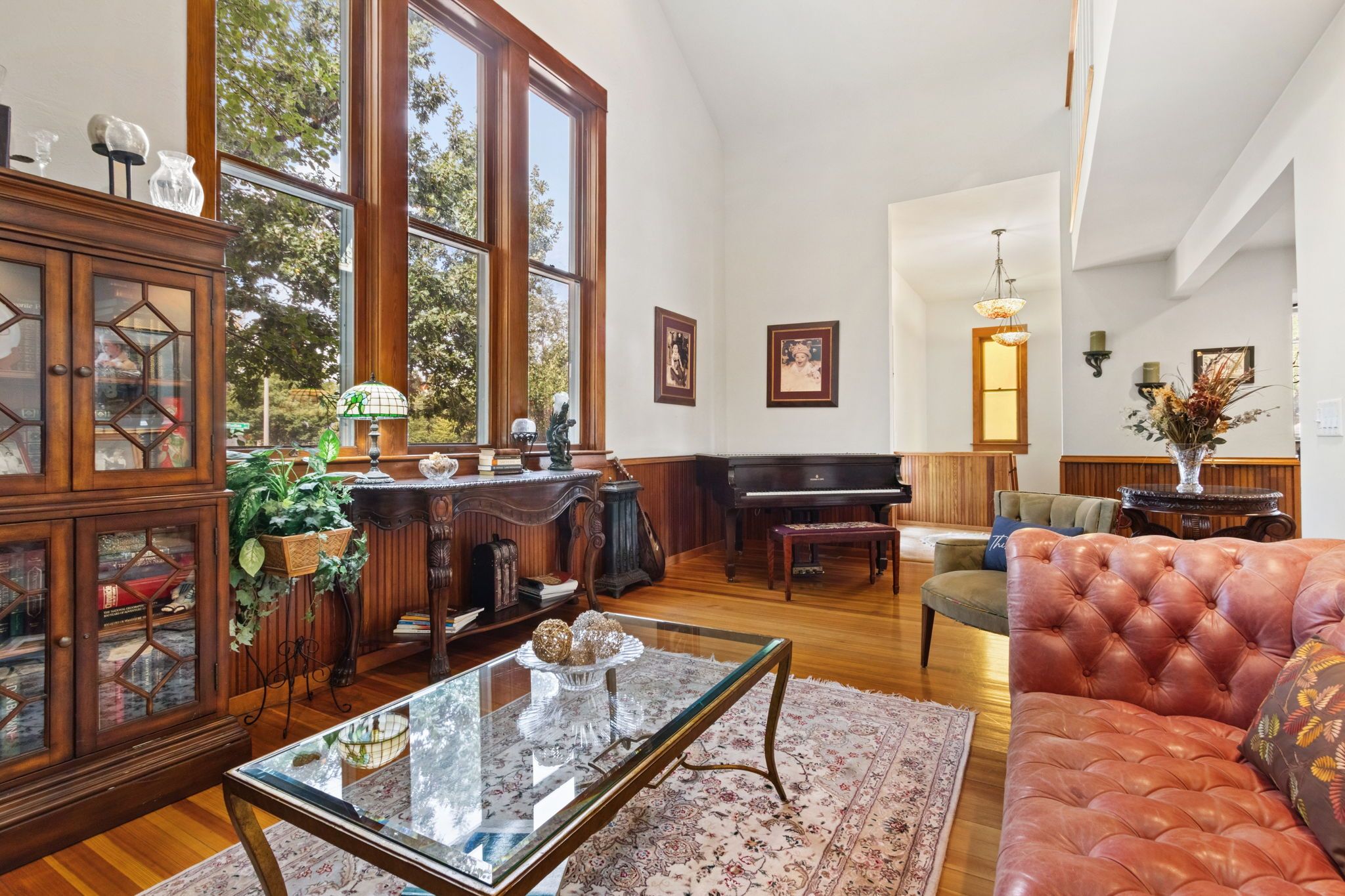 A spacious living room with a grand piano, a glass coffee table, and a leather sofa.