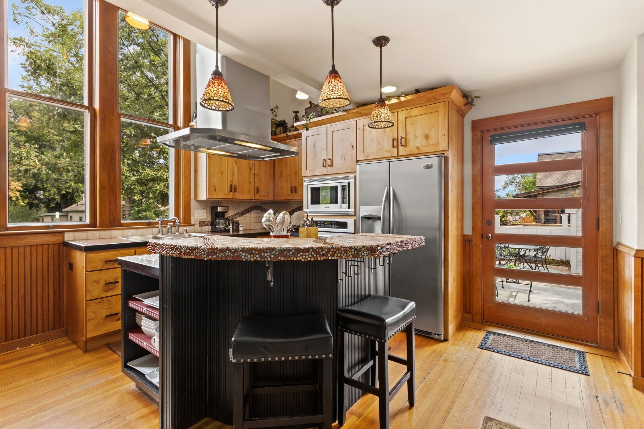 A kitchen with wooden cabinets, a stainless steel refrigerator, a microwave, and a large island with stools.
