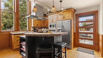 A kitchen with wooden cabinets, a stainless steel refrigerator, a microwave, and a large island with stools.