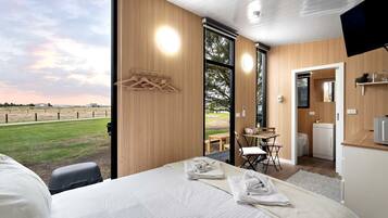 Un dormitorio moderno con una cama grande, un armario de madera, un escritorio con silla y vistas a un campo cubierto de hierba.