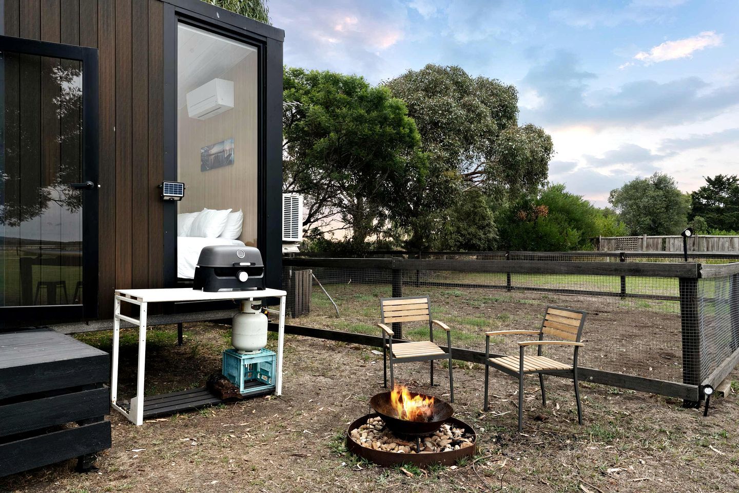An outdoor seating area with a fire pit, a table with a grill, and a view of the surrounding landscape.