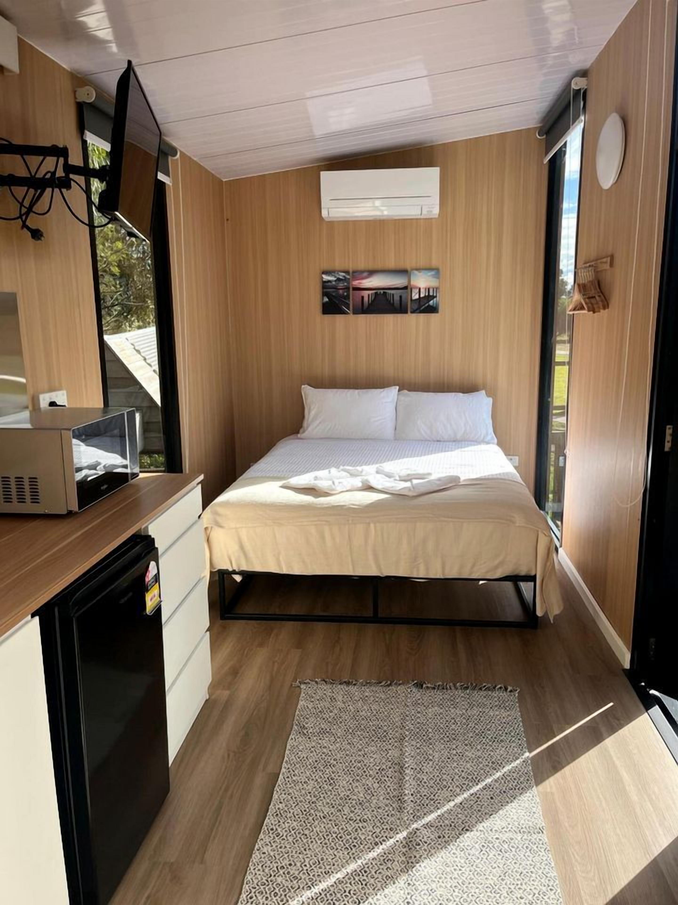 Een kleine kamer met een bed, een bureau met een magnetron en een raam.