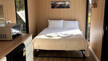 Een kleine kamer met een bed, een bureau met een magnetron en een raam.
