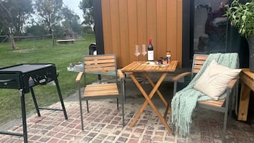 An outdoor patio with a wooden table and chairs, a barbecue grill, and a potted plant.