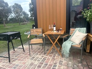 An outdoor patio with a wooden table and chairs, a barbecue grill, and a potted plant.