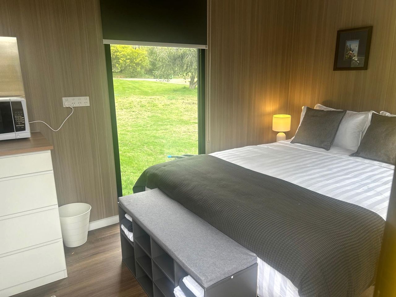 A bedroom with a bed, bedside table, lamp, and a view of the outdoors.