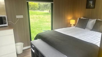 A bedroom with a bed, bedside table, lamp, and a view of the outdoors.