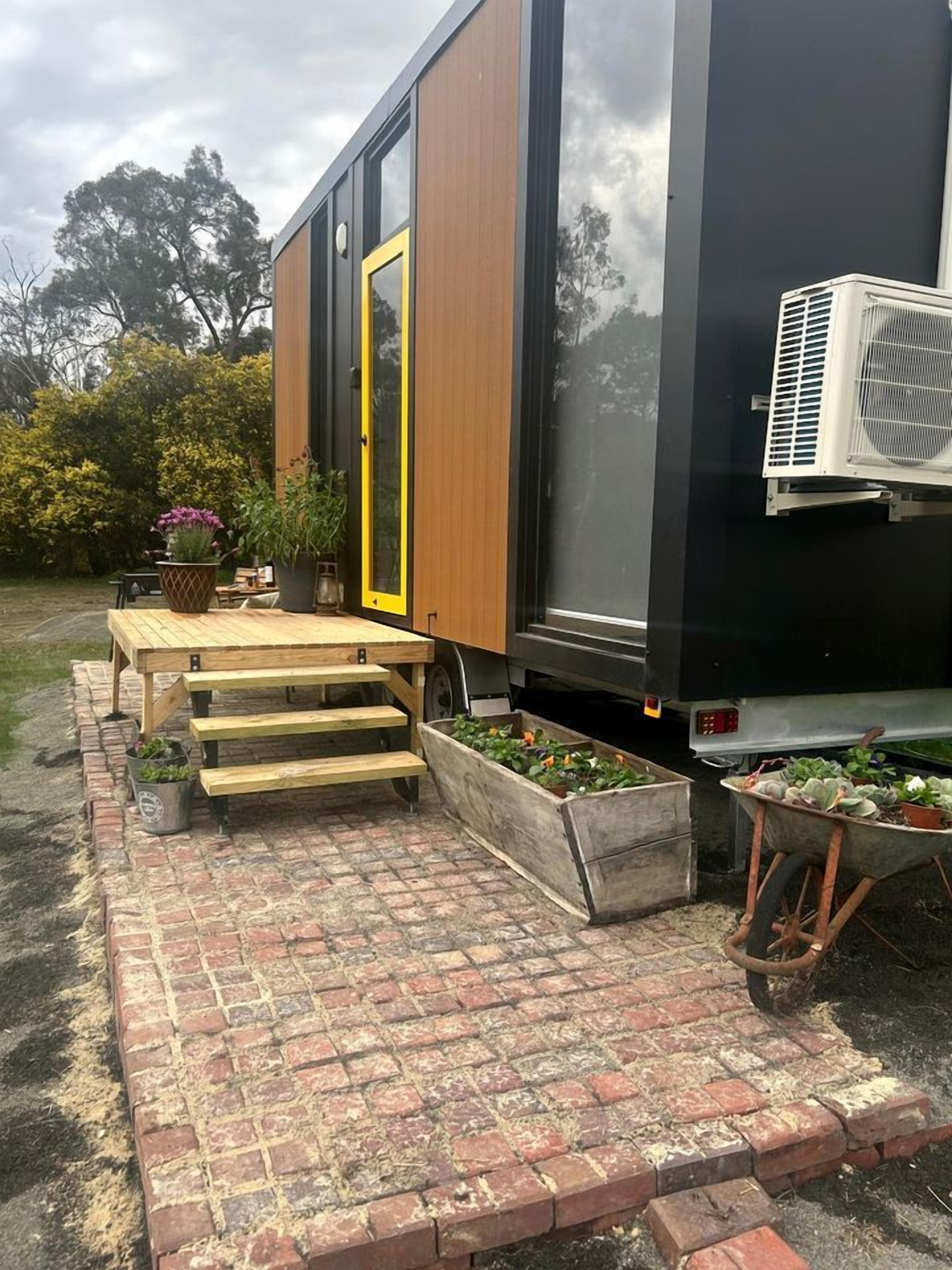 Un bâtiment moderne doté d’une terrasse en bois, d’une porte jaune et d’un mur noir.