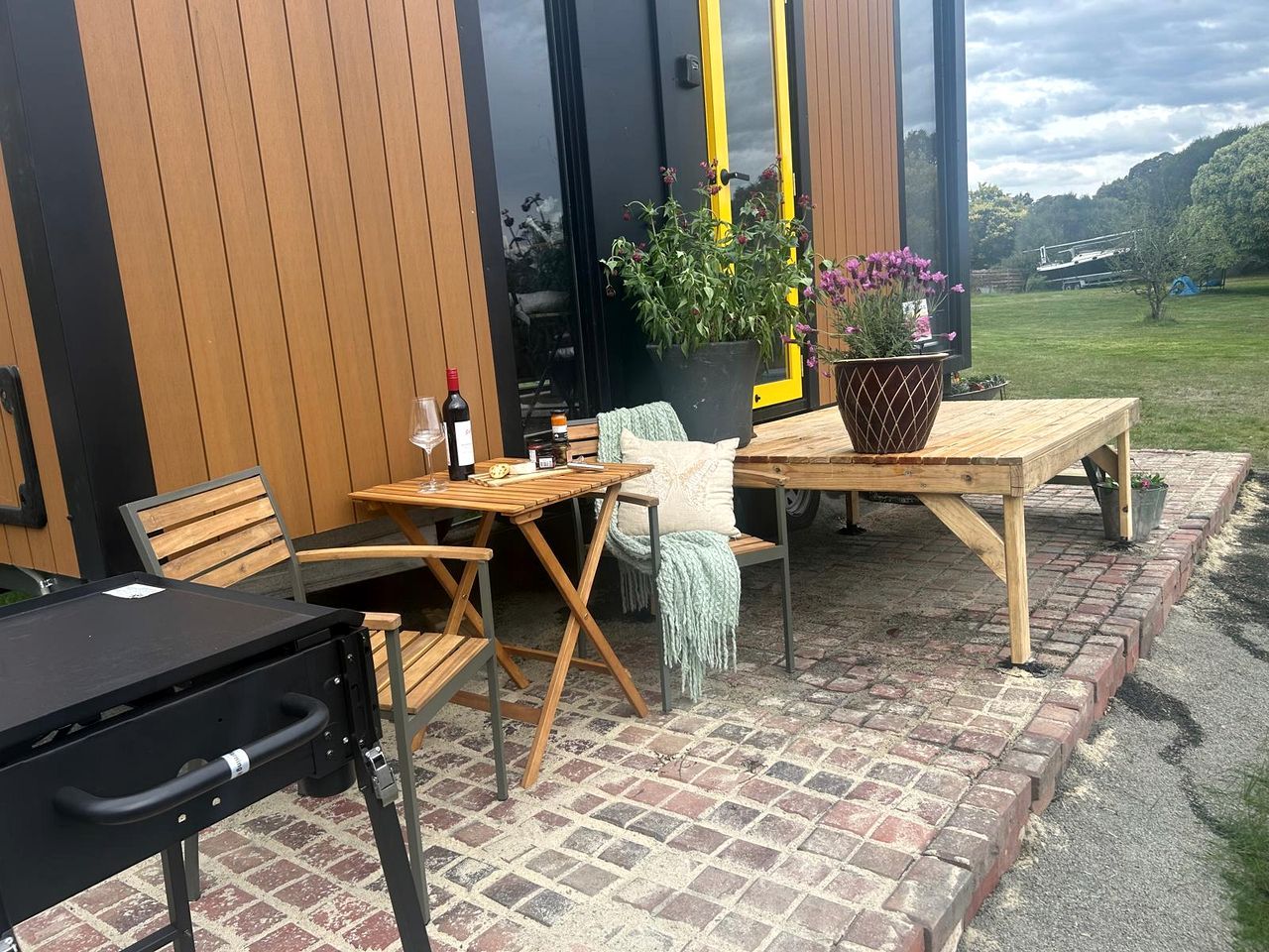 Un espace extérieur aménagé en terrasse, avec une table et des chaises en bois, un banc et un pot de fleurs.