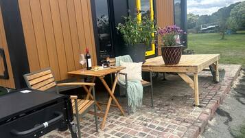 Un espace extérieur aménagé en terrasse, avec une table et des chaises en bois, un banc et un pot de fleurs.