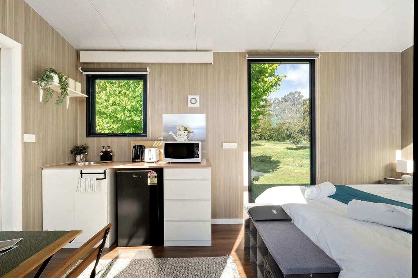 A modern hotel room with a kitchenette, a bed, and a view of the outdoors.