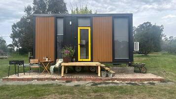 Une maison mobile moderne dotée d’une terrasse en bois, d’une table à manger et de mobilier d’extérieur.