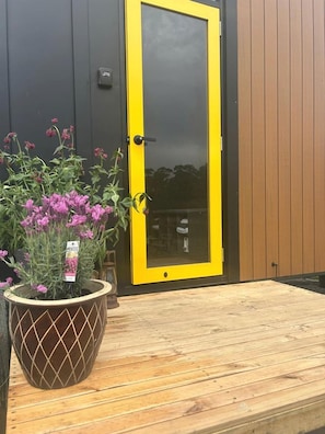 A wooden deck with a potted plant and a yellow door.