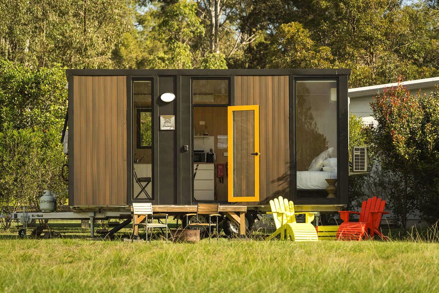 Une petite cabane moderne, avec une façade en bois, une cuisine ouverte et un espace nuit comprenant un lit.