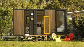 Une petite cabane moderne, avec une façade en bois, une cuisine ouverte et un espace nuit comprenant un lit.