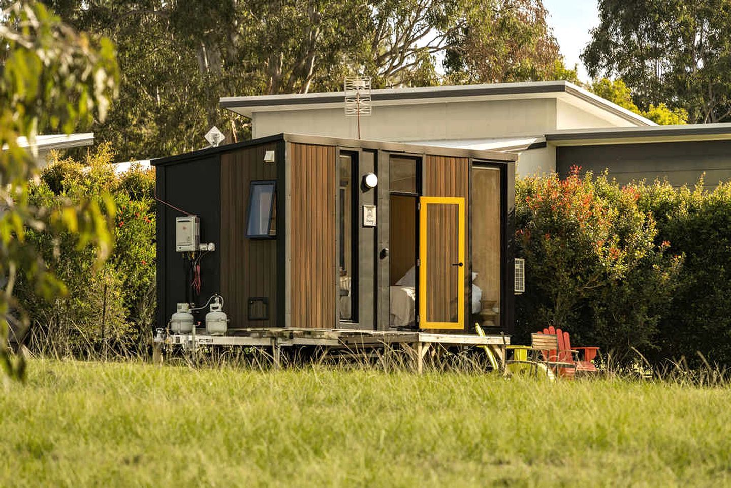 A modern, compact mobile home with a small porch area, a door with a yellow frame, and a satellite dish on the roof.