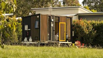 A modern, compact mobile home with a small porch area, a door with a yellow frame, and a satellite dish on the roof.