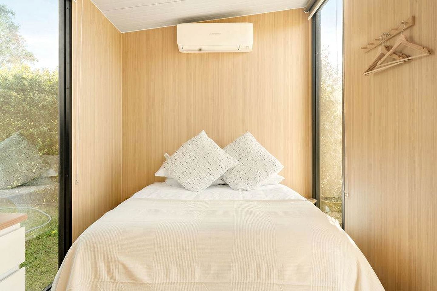 Ein Schlafzimmer mit großem Fenster, einem Bett mit weißer Bettwäsche und einer Holzwand.