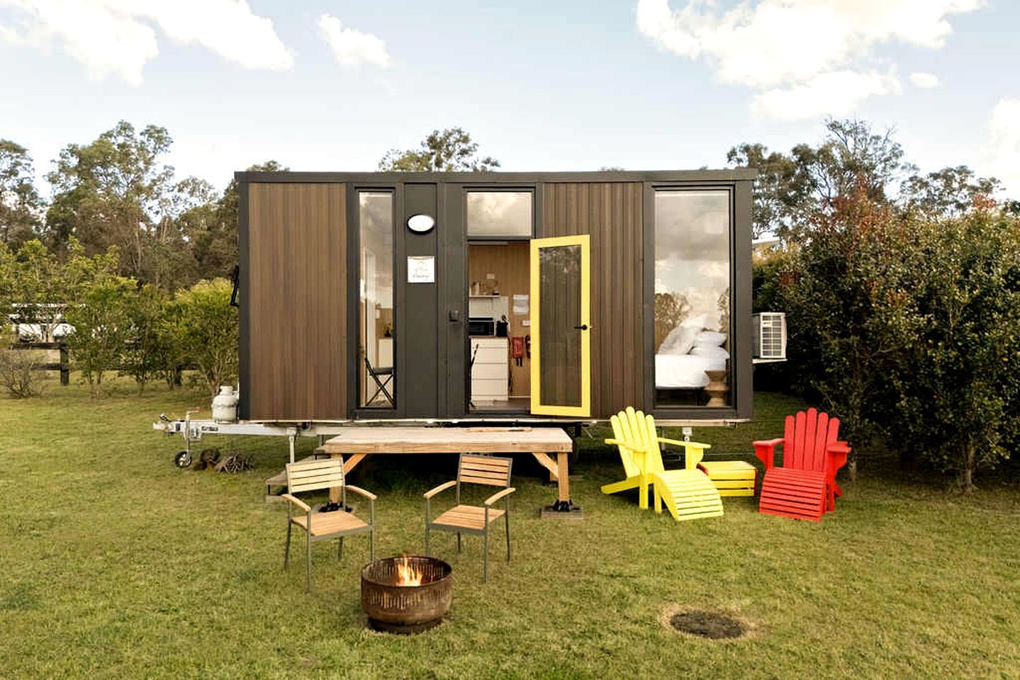 Une maison mobile moderne et compacte, dotée d’un coin cuisine, d’un espace repas avec des chaises et d’un foyer extérieur.