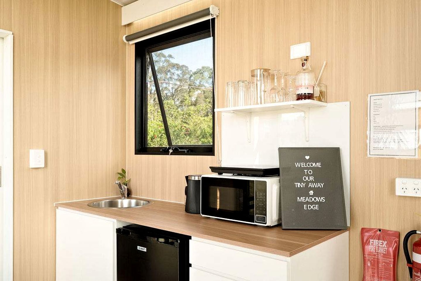 A compact kitchen with a microwave, a sink, and a window with a view of greenery.