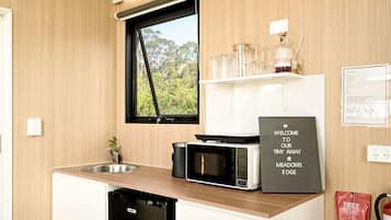 A compact kitchen with a microwave, a sink, and a window with a view of greenery.