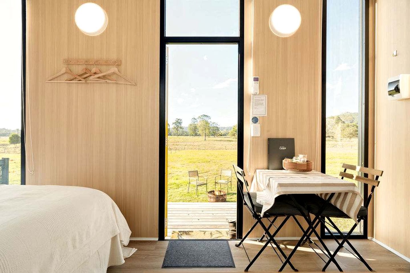 Een kamer met een bed, een tafel met stoelen en uitzicht op een grasveld door een groot raam.