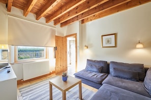 A cozy living room with a wooden ceiling, a sofa, a small table with a plant, and a window with a view of greenery. - Host & Stay | West Loanend Cottage (Berwick-upon-Tweed)