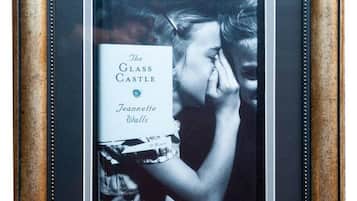 Een ingekaderde foto van een boek, met het gezicht van een persoon, de titel 'The Glass Castle' van Jeannette Walls, en een decoratieve lijst met een metallic afwerking.