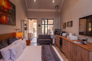 Un dormitorio moderno con una cama grande, un sofá, una chimenea y una zona de cocina con una cafetera.