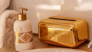 Um banheiro com pia branca, dispensador de sabão dourado e torradeira dourada.