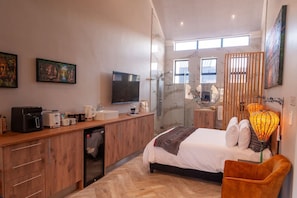 Habitación de hotel moderna con cama, mesita de noche, ducha, escritorio con computadora y obras de arte en las paredes.