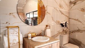 Casa de banho com espelho redondo, lavatório, sanita e porta-toalhas.