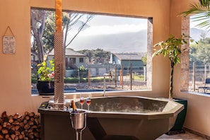 Una habitación con una bañera grande, una ventana con vista a casas, un letrero en la pared y una planta en maceta.
