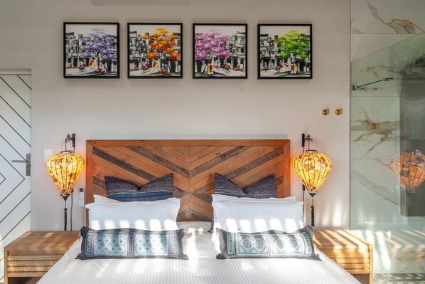 A bedroom with a wooden headboard, two bedside tables, a bed with white bedding, and four framed artworks above the bed.