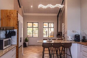 Una cocina moderna con una isla central, taburetes de bar, horno empotrado y un amplio ventanal que proporciona luz natural.