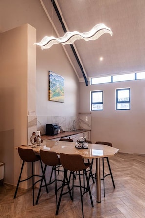 Eine moderne Küche mit Essbereich, ausgestattet mit einem großen Tisch und Stühlen, einer Hängeleuchte und einem Gemälde an der Wand.