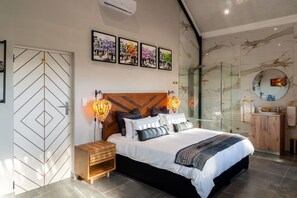 Un dormitorio moderno con una cama, mesitas de noche, ducha de vidrio y obras de arte en las paredes.