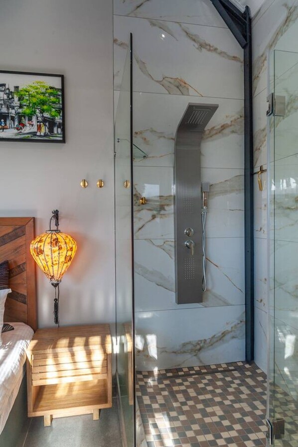 A modern bathroom with a glass shower enclosure, a marble wall, and a checkered floor.