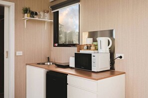 Una kitchenette compacta con microondas, tostadora y cafetera sobre una encimera de madera.