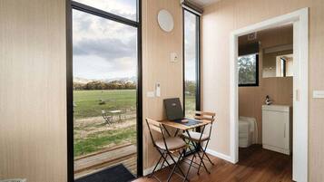 A room with a view of a grassy field, a small table with a laptop, and a compact kitchenette.
