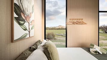 Ein Schlafzimmer mit großem Fenster, einem Bett mit Kissen, einem Bild an der Wand und einem Holzregal.