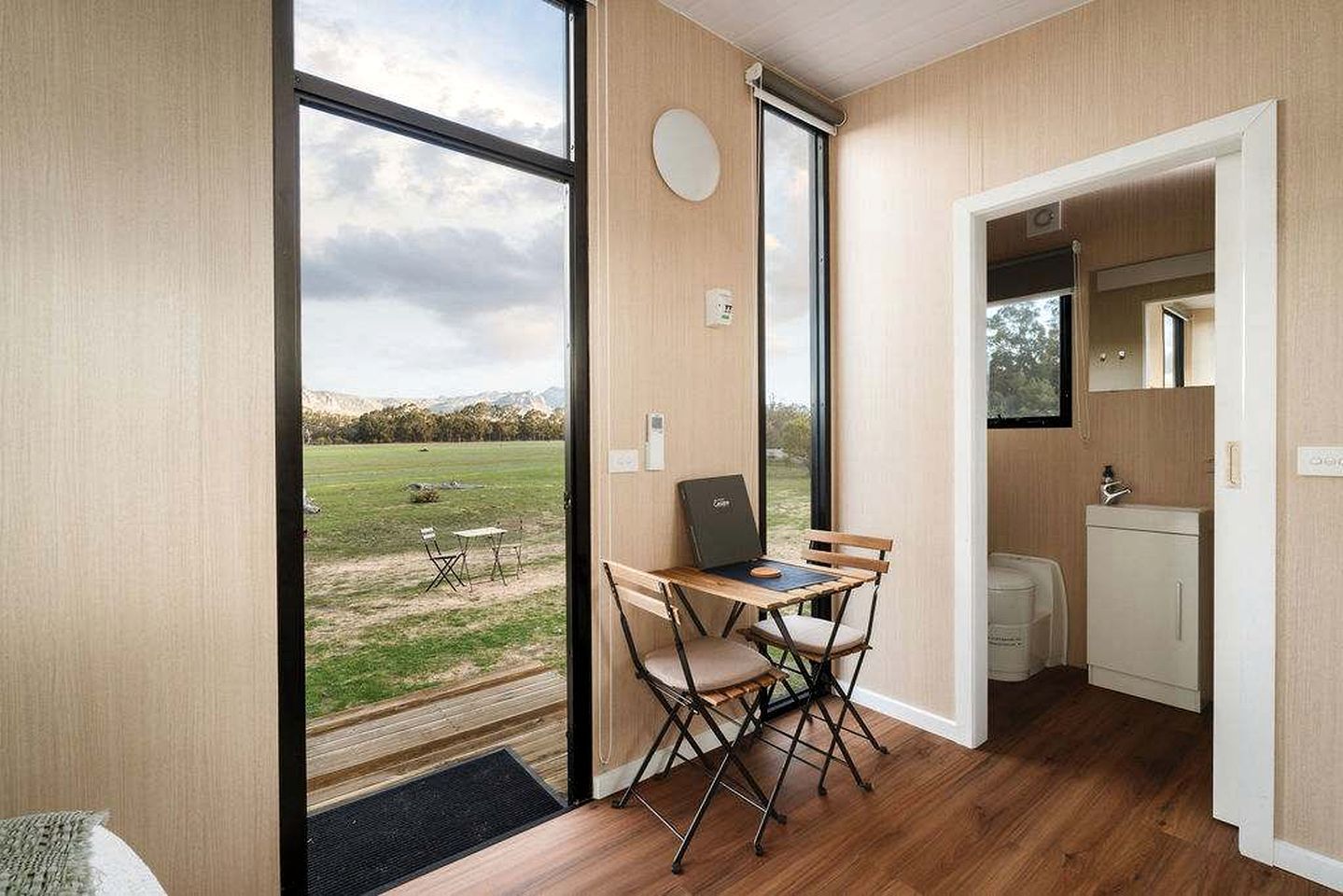 Una habitación con vistas a un campo cubierto de césped, una mesita con una computadora portátil y una kitchenette pequeña.