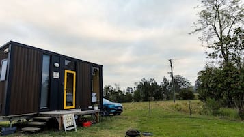 Una casa móvil moderna y compacta, con una puerta amarilla distintiva, ubicada en una zona con césped y un coche azul estacionado cerca.