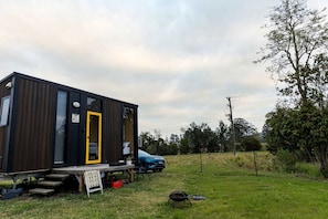 Una casa móvil moderna y compacta, con una puerta amarilla distintiva, ubicada en una zona con césped y un coche azul estacionado cerca.