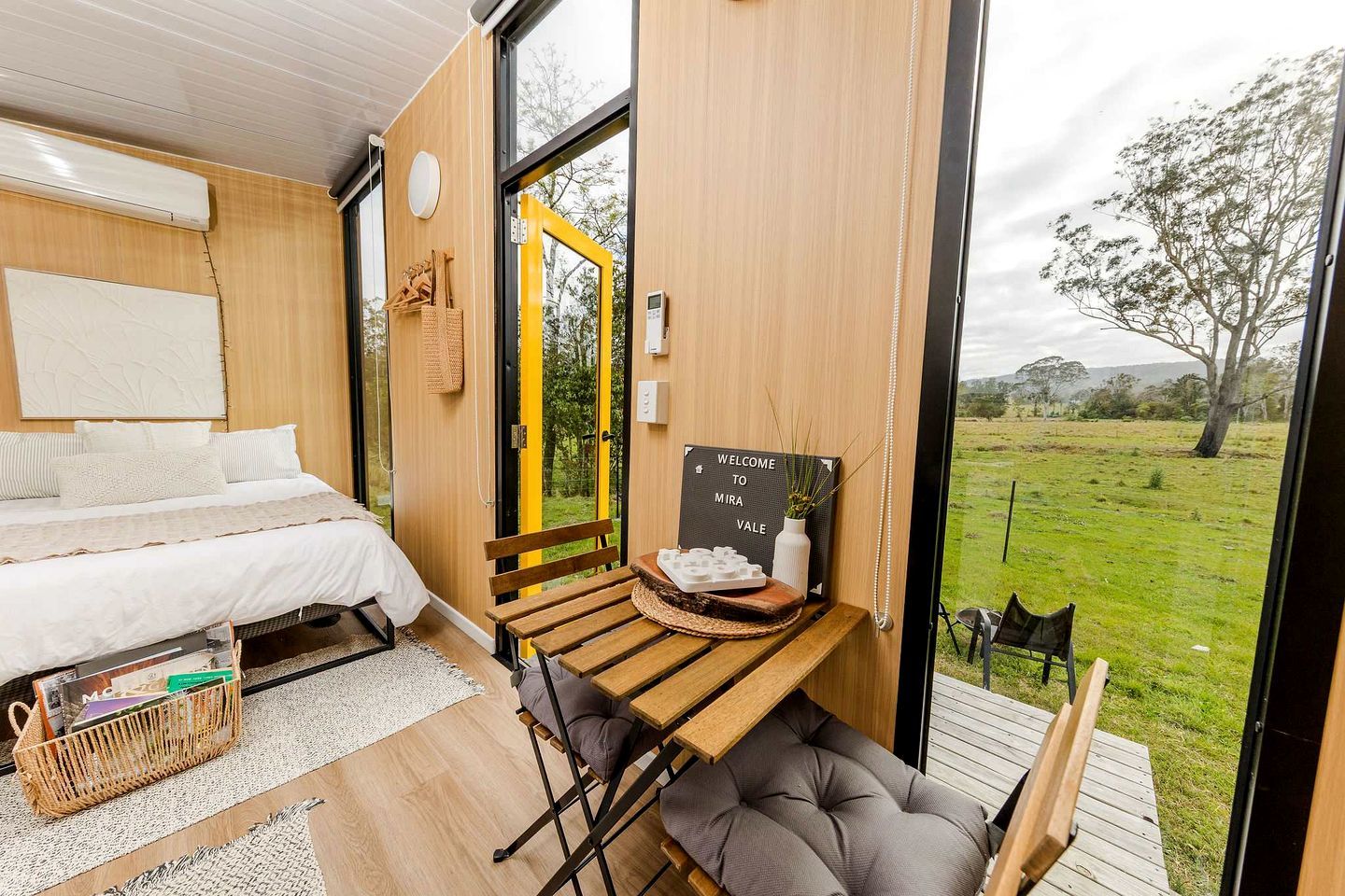 Un dormitorio moderno con una cama, una mesita con un letrero, un banco y vistas a un campo cubierto de césped.