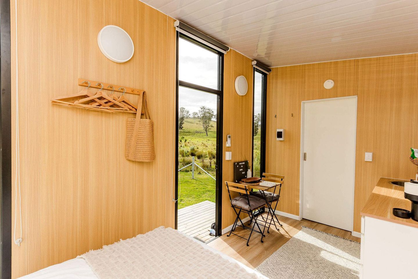 Una habitación moderna con paredes de madera, una cama, un escritorio con silla y vistas a un paisaje verde a través de un ventanal.